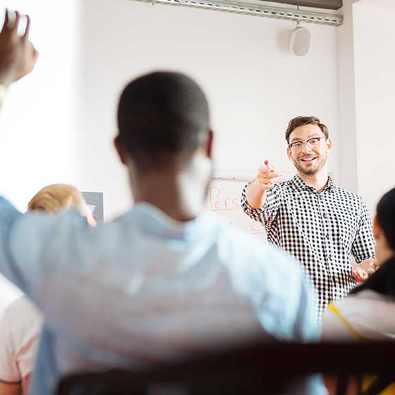 A photo of a young white man pointing towards a black man in the foreground who's back is facing the camera.