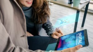 A woman and a man are looking at a tablet computer screen. The screen has the words digital transformation written on it. There are graphics of charts.