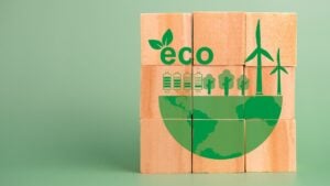 Nine wooden blocks on a green background are stacked in a three by three formation. On the block are green graphics representing the earth trees, wind power and electric. the word eco with a green leaf growing from it is printed on the blocks.
