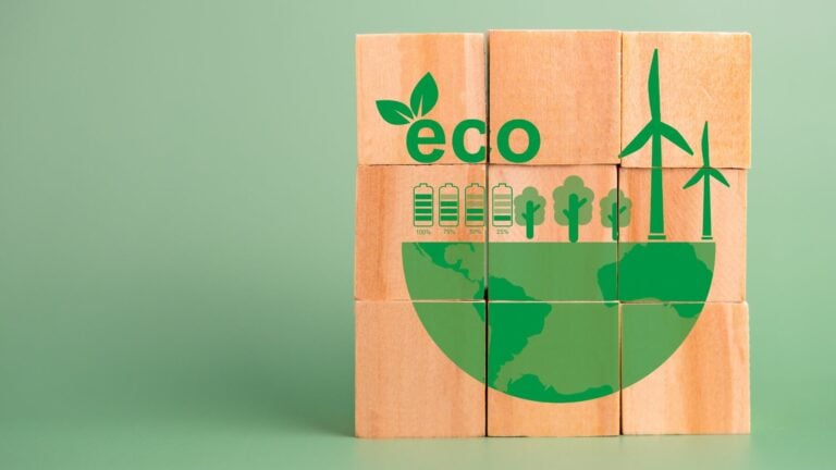 Nine wooden blocks on a green background are stacked in a three by three formation. On the block are green graphics representing the earth trees, wind power and electric. the word eco with a green leaf growing from it is printed on the blocks.