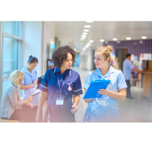 Two women working in a hospital. One women is holding a clipboard and showing it to the other.