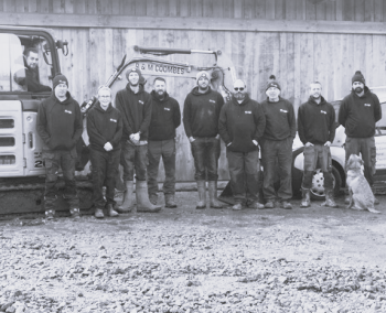 Black and white image of ten R and M Coombes employees stood in a line, with one of them sat in a forklift.