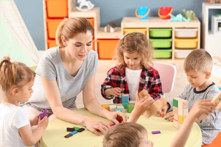 A woman and four children sat around a table doing arts and crafts in a school setting.