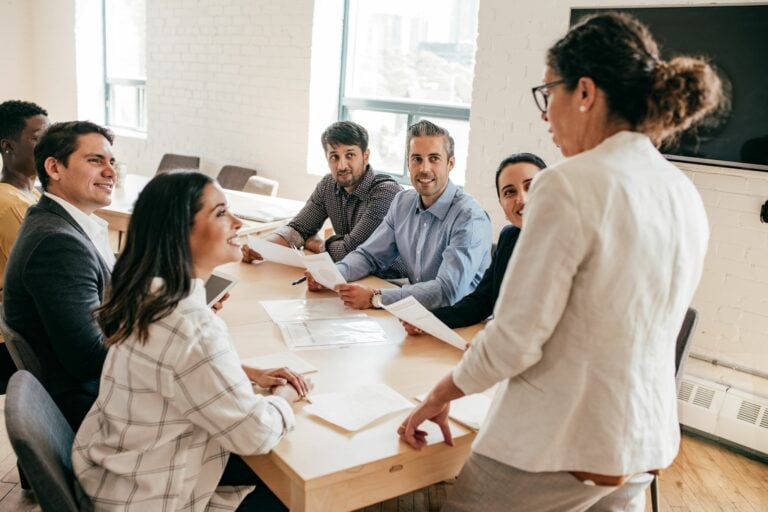 A woman stood at the head of a table talking to a group sat down