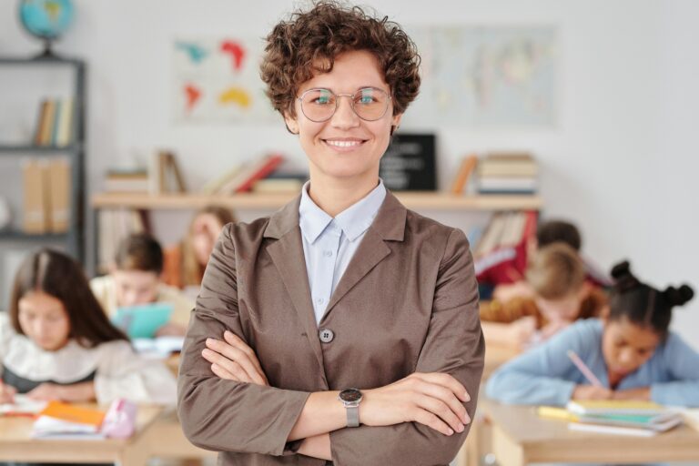 A school teacher stood in front of a classroom smiling at the camera